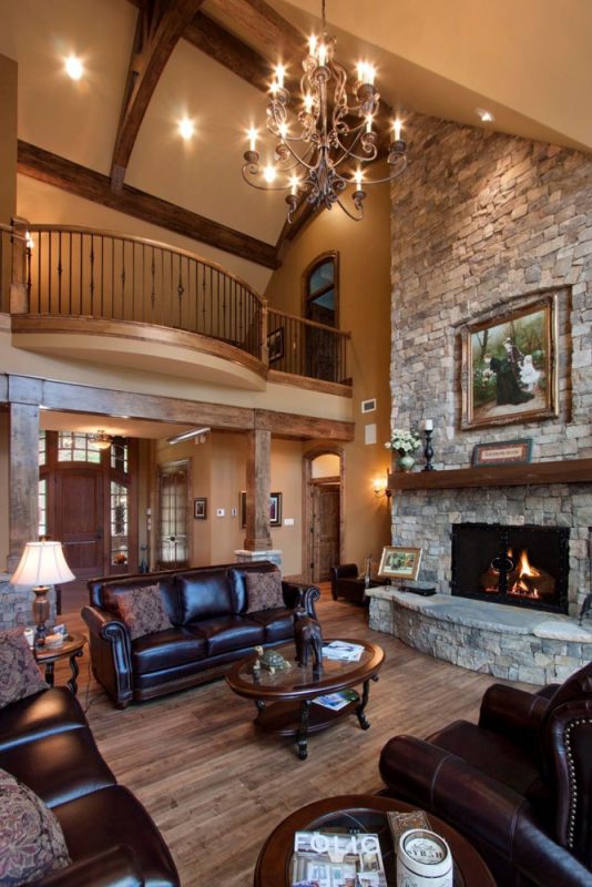 Grand living room with two-story vaulted ceiling, stone fireplace, wrought iron balcony, and exposed timber beams – Buchanan Construction, Asheville.