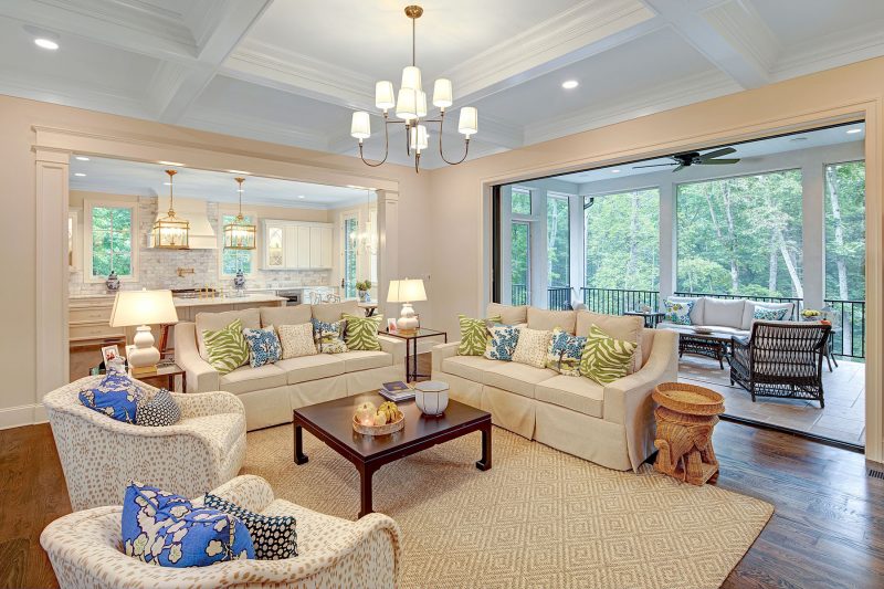 Open concept living room with cream-colored sofas, armchairs, and coffered ceiling, leading to a screened porch – Buchanan Construction Asheville NC